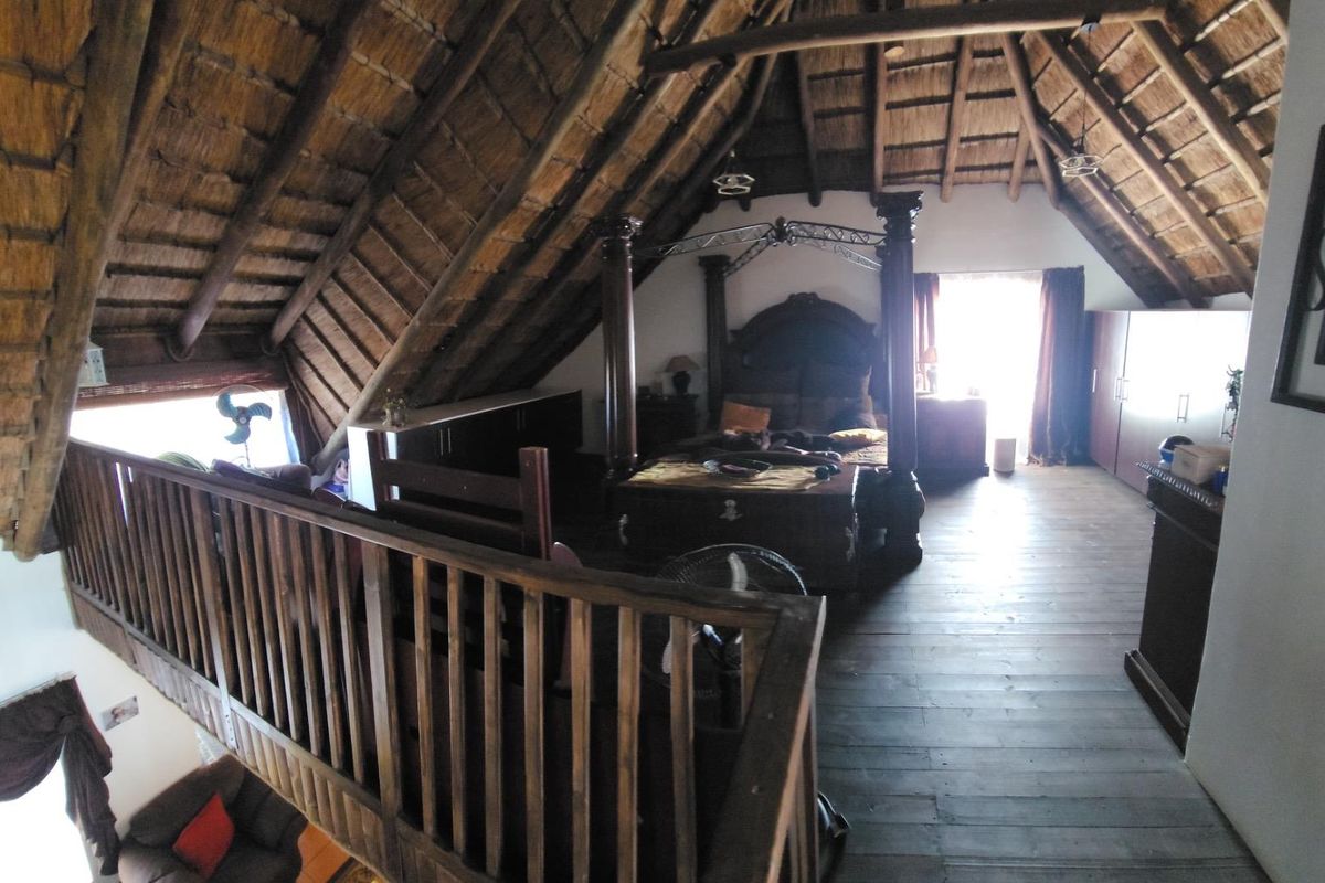 Spacious loft-style bedroom featuring exposed timber roof trusses, a traditional thatched ceiling, and warm timber flooring with a mezzanine overlook.