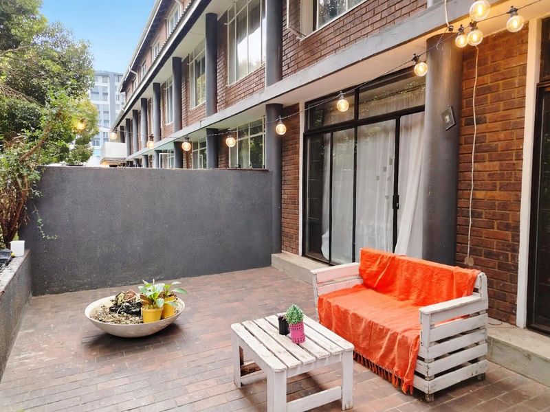 A private ground-floor patio featuring brick paving, a solid retaining wall, and direct access to the apartment interior through sliding glass doors.
