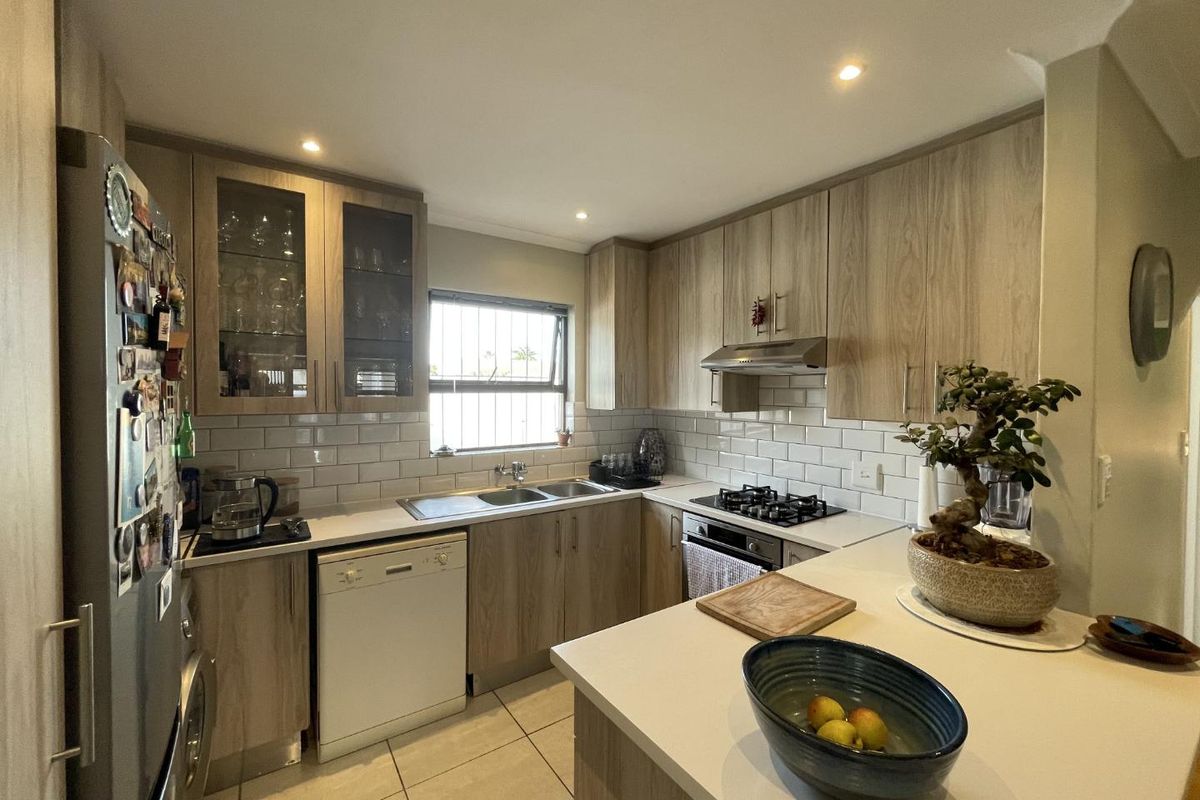 Modern kitchen featuring light wood-grain cabinetry, subway tile backsplash, stone countertops, and integrated gas hob with extractor fan.