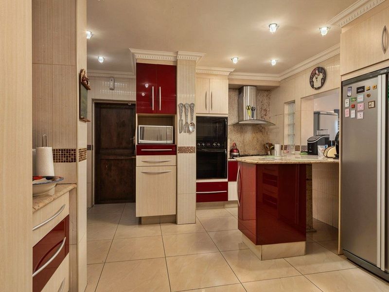 A well-appointed kitchen featuring high-gloss cabinetry, granite countertops, built-in oven, extractor fan, and tiled flooring with recessed lighting.