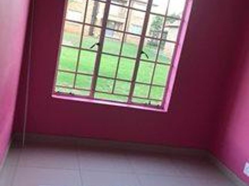An empty bedroom featuring tiled flooring and a large window with security bars, offering a view of the exterior grounds.