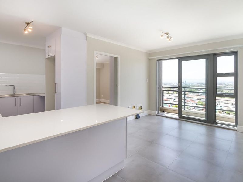 Modern open-plan living area featuring a sleek kitchen with quartz countertops, tiled flooring, and large sliding doors leading to a balcony with city views.
