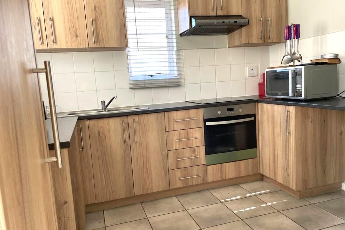 Functional kitchen featuring wood-look cabinetry, dark laminate countertops, built-in oven, extractor fan, and tiled flooring with a window for natural light.