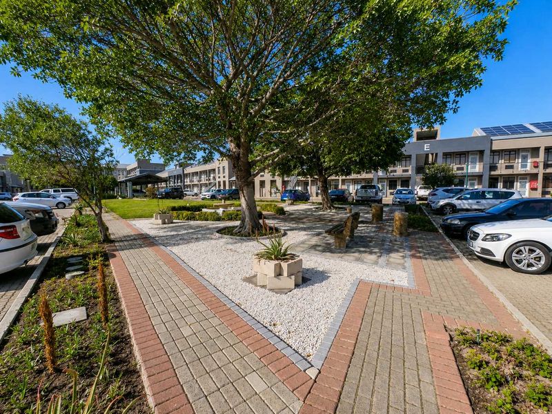 A well-maintained office park exterior featuring paved parking areas, landscaped garden beds, and mature trees providing shade to the communal outdoor space.
