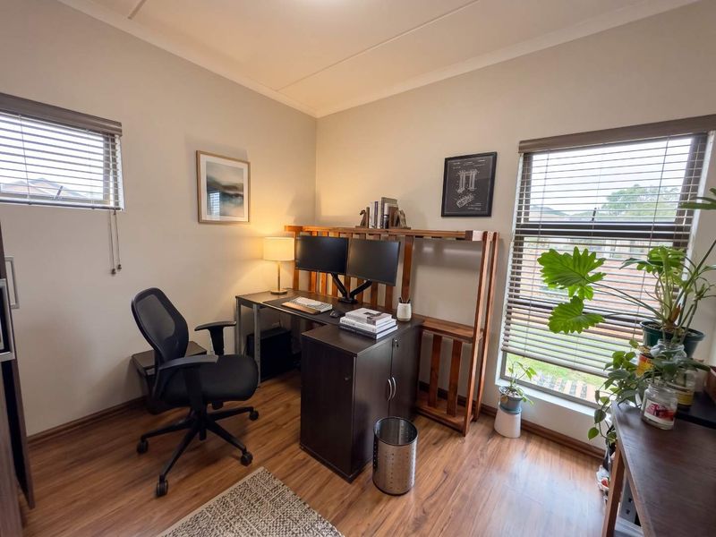A bright home office featuring laminate flooring and dual windows with fitted venetian blinds, providing a functional workspace.