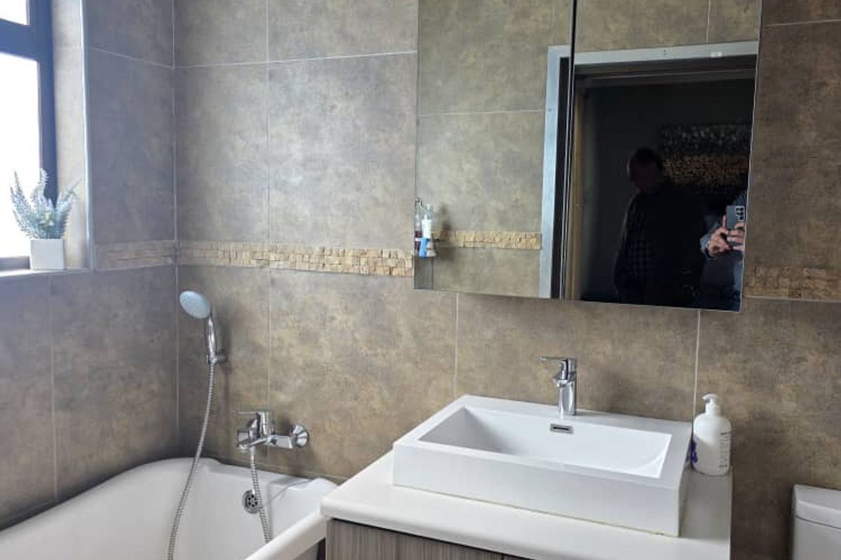 Modern bathroom featuring a freestanding bathtub, wall-mounted vanity with vessel sink, mirrored medicine cabinet, and neutral ceramic wall tiling with a decorative mosaic border.
