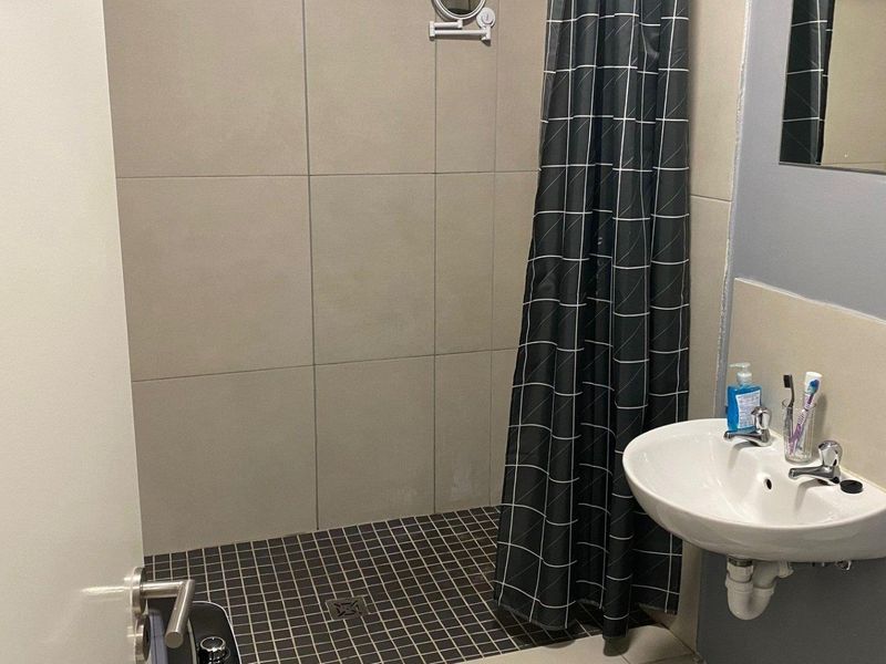 Compact bathroom featuring a walk-in shower with tiled finishes and a wall-mounted basin.