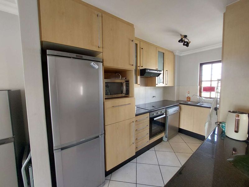 A functional kitchen featuring light wood cabinetry, dark countertops, stainless steel appliances, and tiled flooring, offering a practical layout for daily cooking.