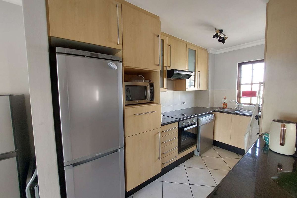 A functional kitchen featuring light wood cabinetry, dark countertops, stainless steel appliances, and tiled flooring, offering a practical layout for daily cooking.