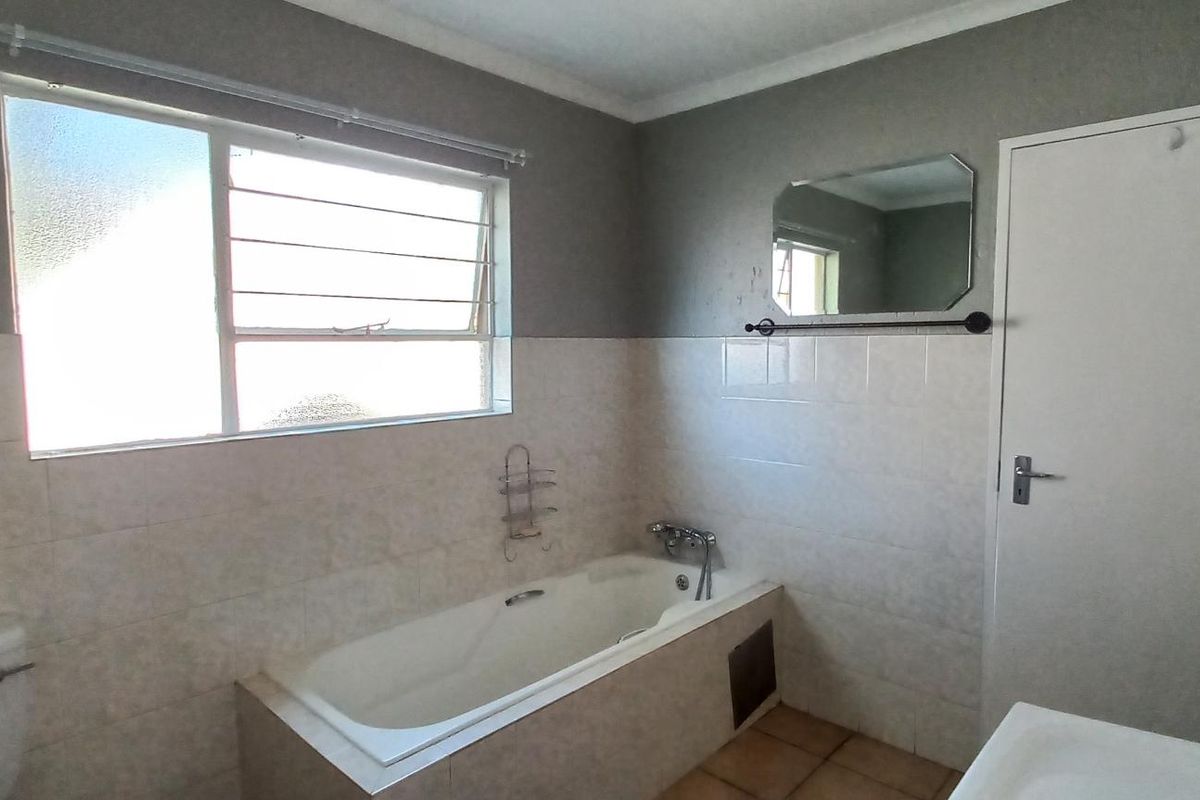A functional bathroom featuring a built-in bathtub, tiled walls, and louvered windows, offering a clean canvas for potential modern updates.