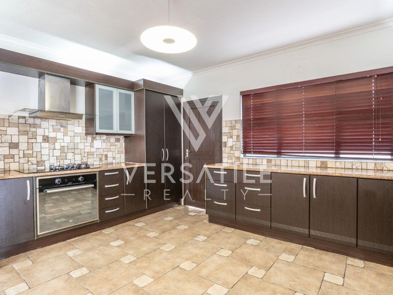 A well-maintained kitchen featuring dark wood cabinetry, granite countertops, stone tile flooring, and built-in appliances including a gas hob and oven.