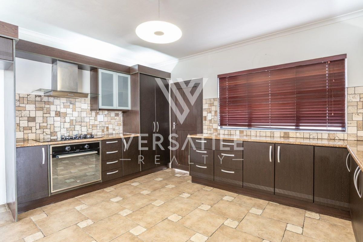 A well-maintained kitchen featuring dark wood cabinetry, granite countertops, stone tile flooring, and built-in appliances including a gas hob and oven.
