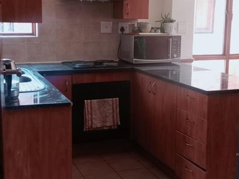 A functional kitchen featuring wooden cabinetry, granite countertops, a built-in oven, and an electric hob with a tiled backsplash and flooring.