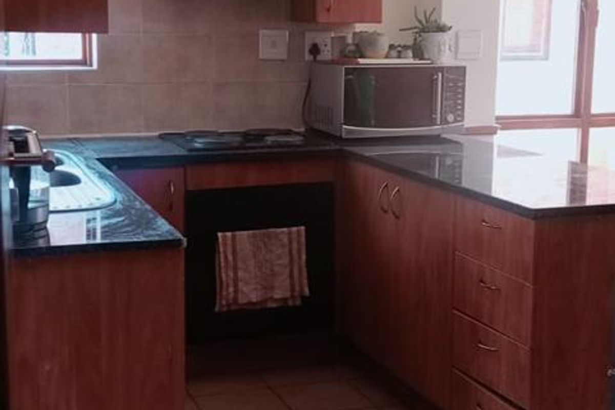 A functional kitchen featuring wooden cabinetry, granite countertops, a built-in oven, and an electric hob with a tiled backsplash and flooring.