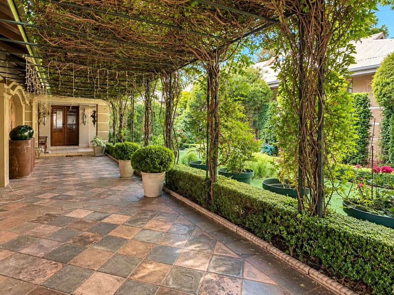 A covered patio area featuring decorative tiled flooring and a metal pergola structure with established climbing plants, leading to the main entrance.