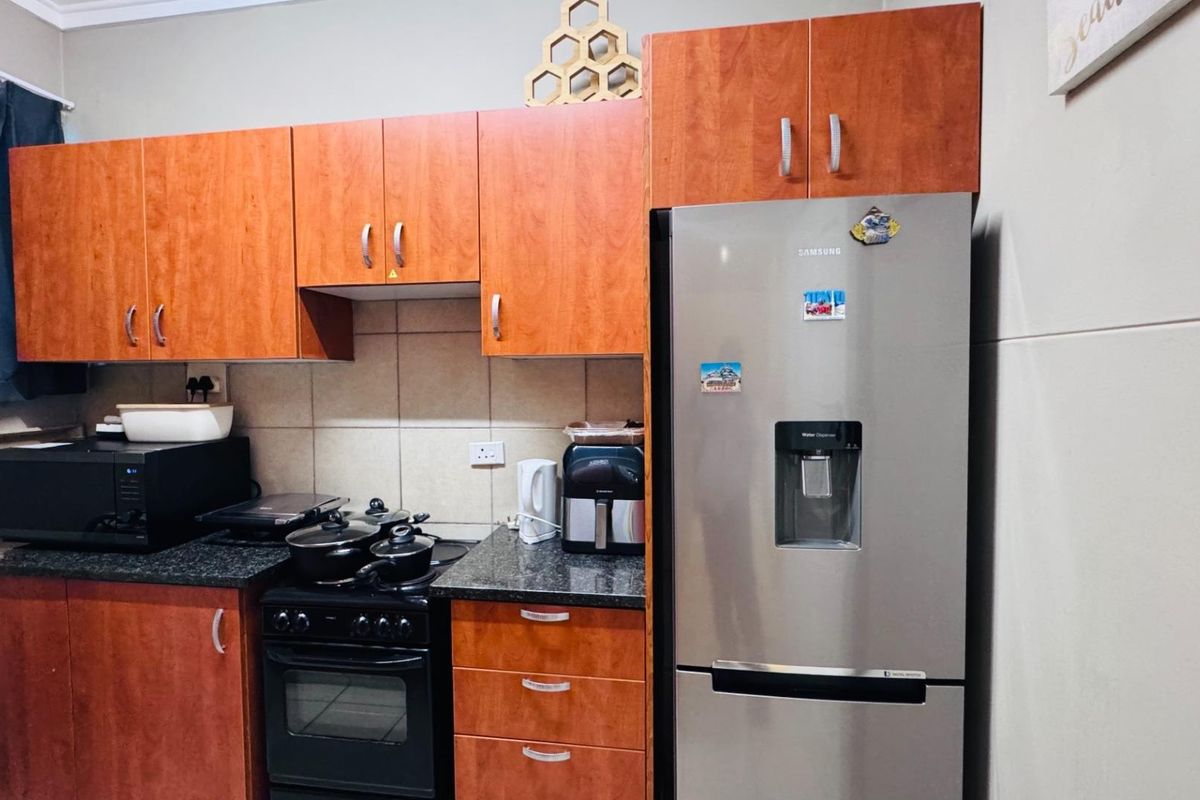 A functional kitchen featuring wood-finish cabinetry, granite countertops, a tiled backsplash, and a freestanding oven with hob.