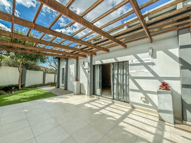 A spacious tiled patio area featuring a timber pergola, sliding glass doors, and access to a private garden space.