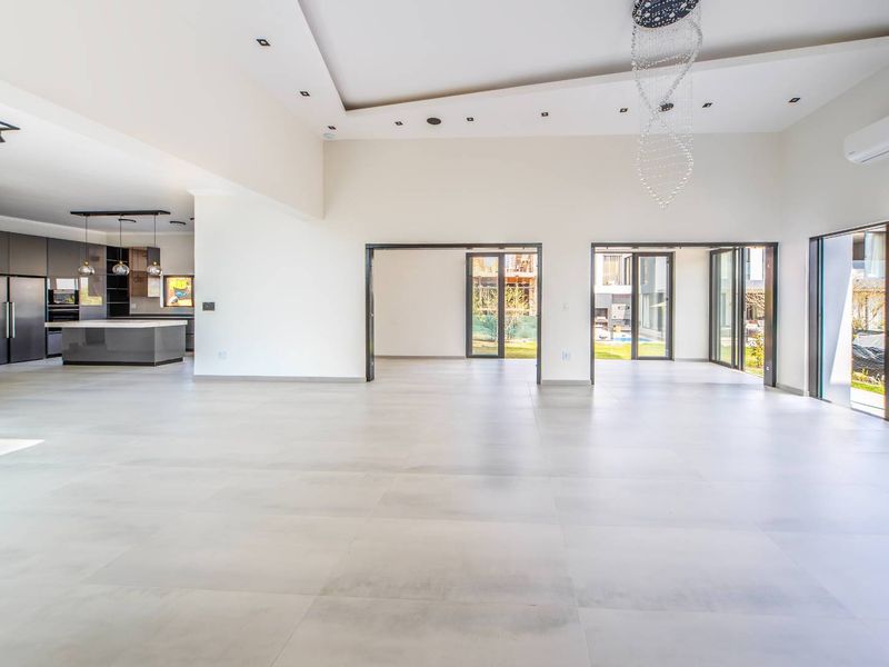 Spacious open-plan living area featuring large format floor tiles, recessed lighting, and seamless flow to the outdoor patio through expansive sliding glass doors.