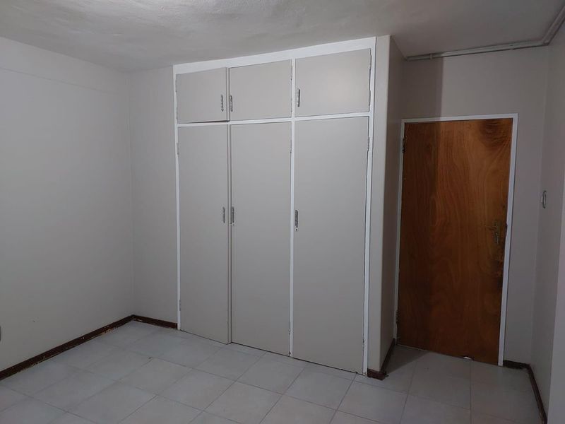 A bedroom featuring built-in cupboards with overhead storage and tiled flooring.