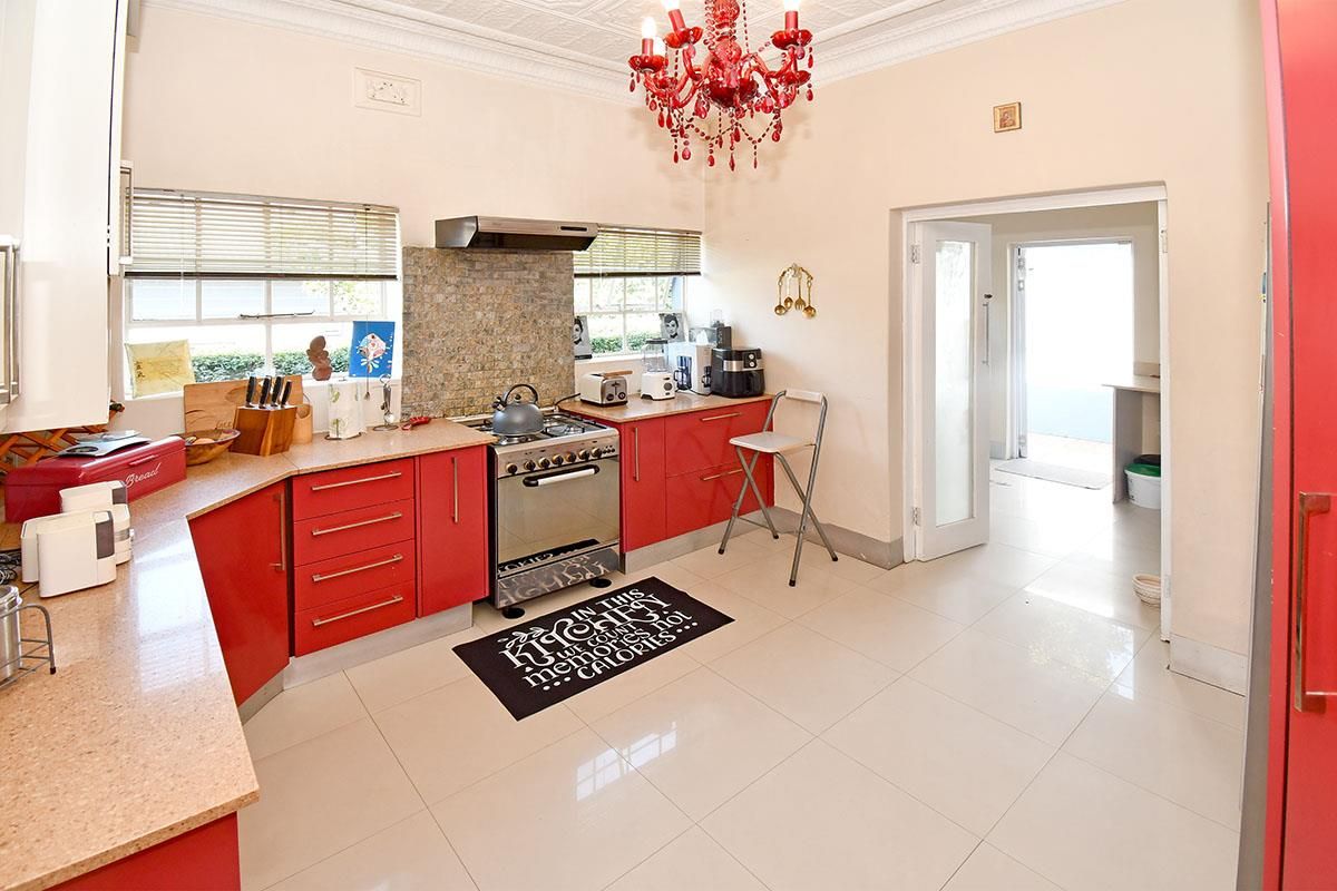A functional kitchen featuring red cabinetry, a stainless steel gas stove with extractor fan, tiled flooring, and a decorative chandelier.