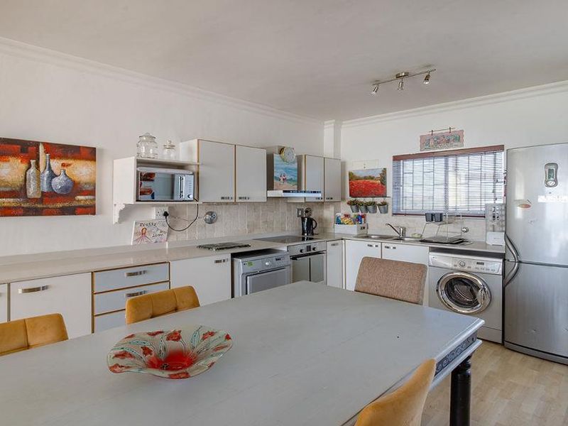 Open-plan kitchen and dining area featuring white cabinetry, laminate countertops, tiled backsplash, built-in oven, and integrated laundry appliances.