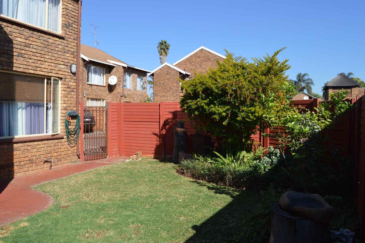 A private rear garden featuring a lawn, paved patio area, and face brick exterior walls, enclosed by timber fencing and a metal gate.