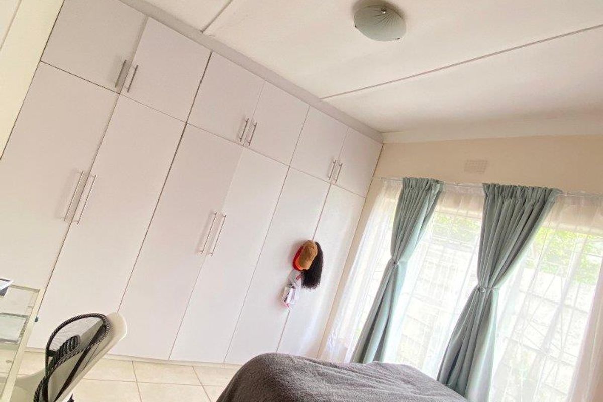 A well-lit bedroom featuring extensive floor-to-ceiling built-in cupboards and neutral tiled flooring, providing ample storage and a clean, functional living space.