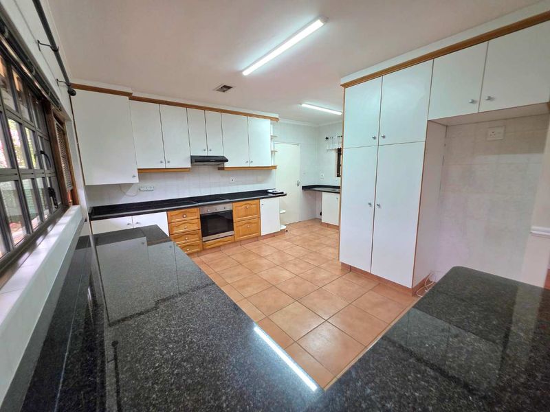 Spacious kitchen featuring granite countertops, built-in cabinetry, integrated oven, and extractor fan with tiled flooring throughout.