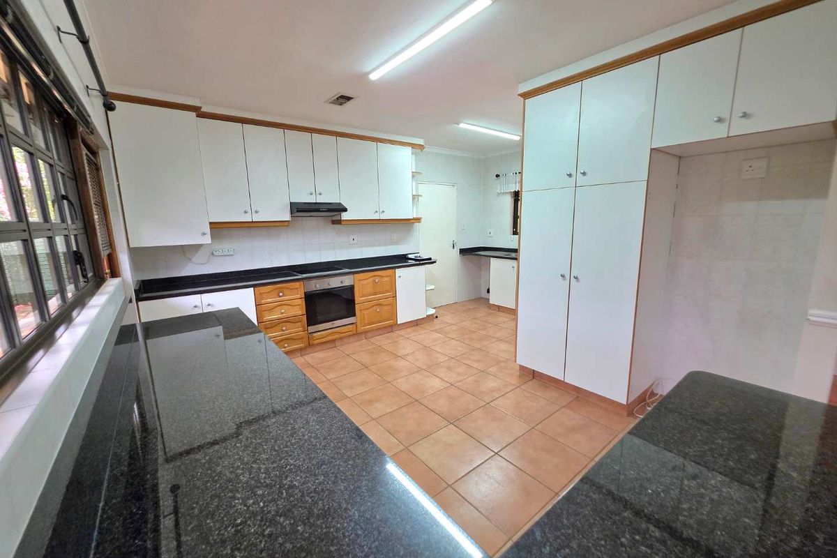 Spacious kitchen featuring granite countertops, built-in cabinetry, integrated oven, and extractor fan with tiled flooring throughout.