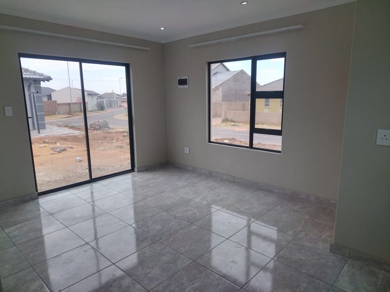 A bright, empty living area featuring modern grey tiled flooring, aluminium window frames, and a sliding door providing natural light and street views.