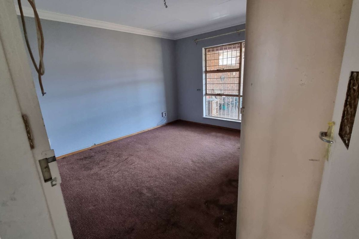 An empty bedroom featuring brown carpeting, a window with security bars, and crown molding, requiring cosmetic updates and repairs.