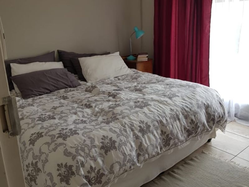 A functional bedroom featuring tiled flooring, a wall-mounted split-system air conditioner, and a ceiling fan, providing a comfortable and practical living space.