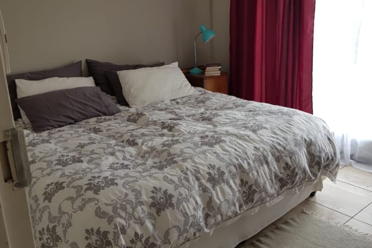 A functional bedroom featuring tiled flooring, a wall-mounted split-system air conditioner, and a ceiling fan, providing a comfortable and practical living space.
