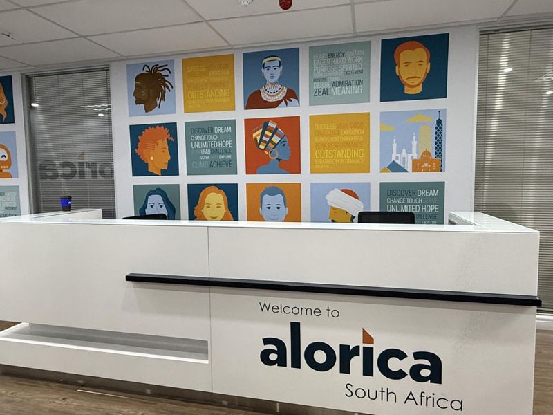 A professional office reception area featuring a branded reception desk, modern laminate flooring, and a decorative feature wall with graphic artwork.