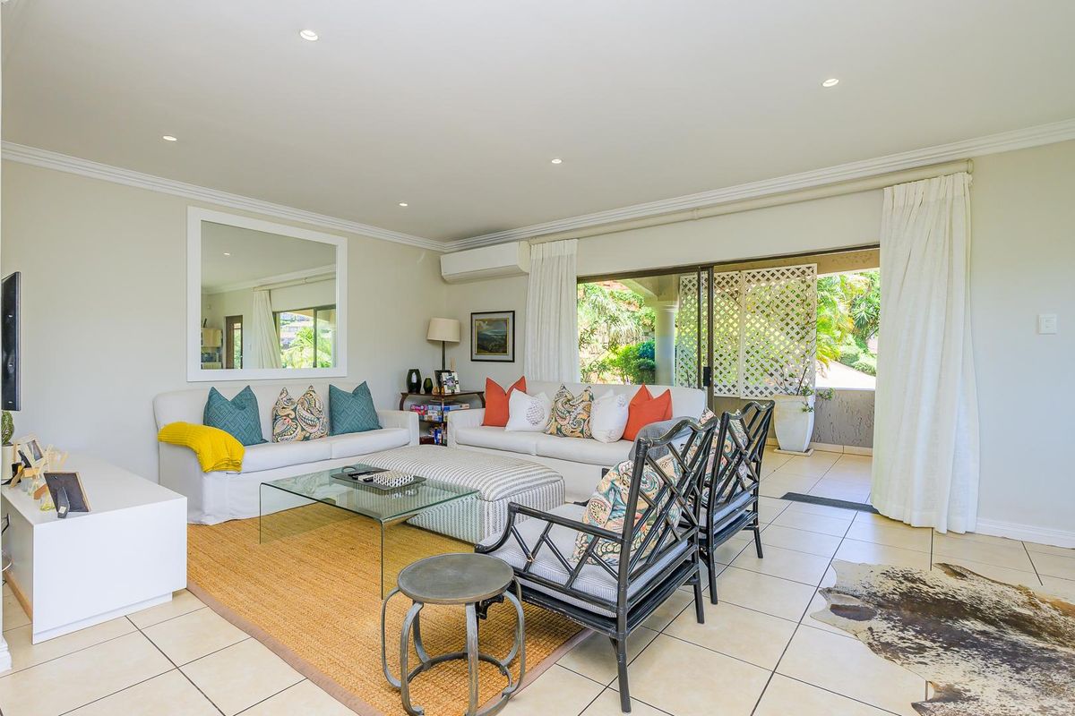 A bright and spacious living room featuring tiled flooring, recessed downlighting, and large sliding glass doors that open onto a covered patio area.
