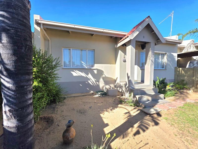 Front elevation of a townhouse featuring a covered entrance porch, concrete steps, and established garden area with security window bars.
