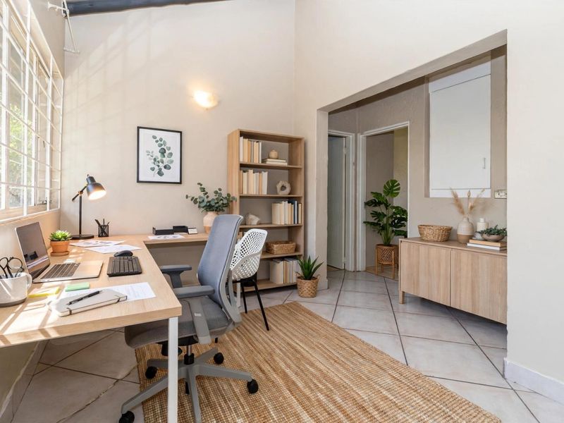 A bright and functional home office space featuring tiled flooring, a vaulted ceiling, and large windows that provide ample natural light.