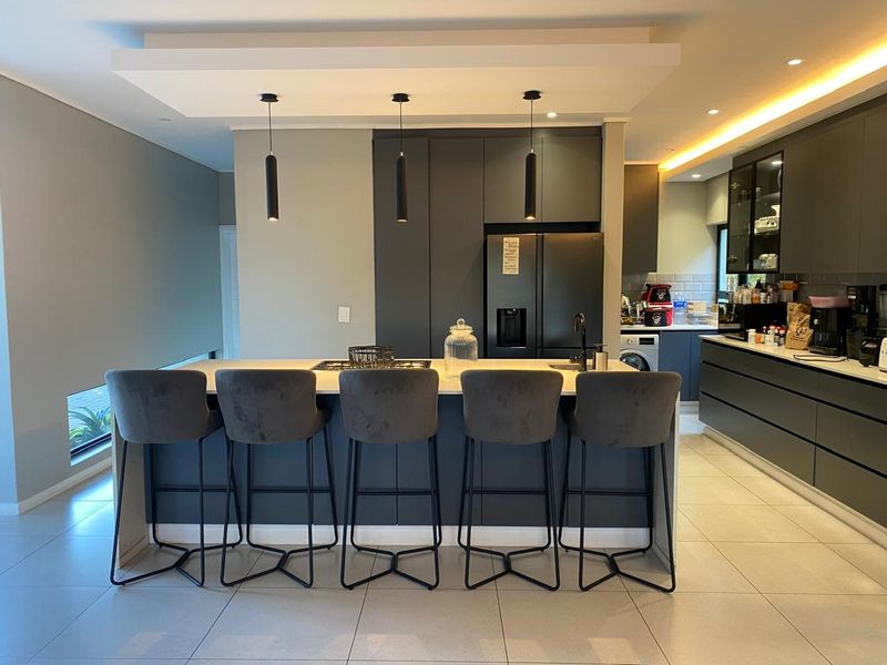 Modern open-plan kitchen featuring a large central island with integrated hob, sleek dark cabinetry, stone countertops, and recessed ceiling lighting.