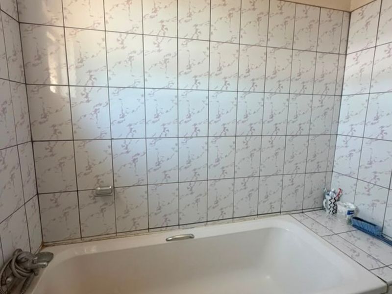 A functional bathroom featuring a built-in bathtub with tiled surround and wall cladding, requiring minor maintenance to grout and sealant.