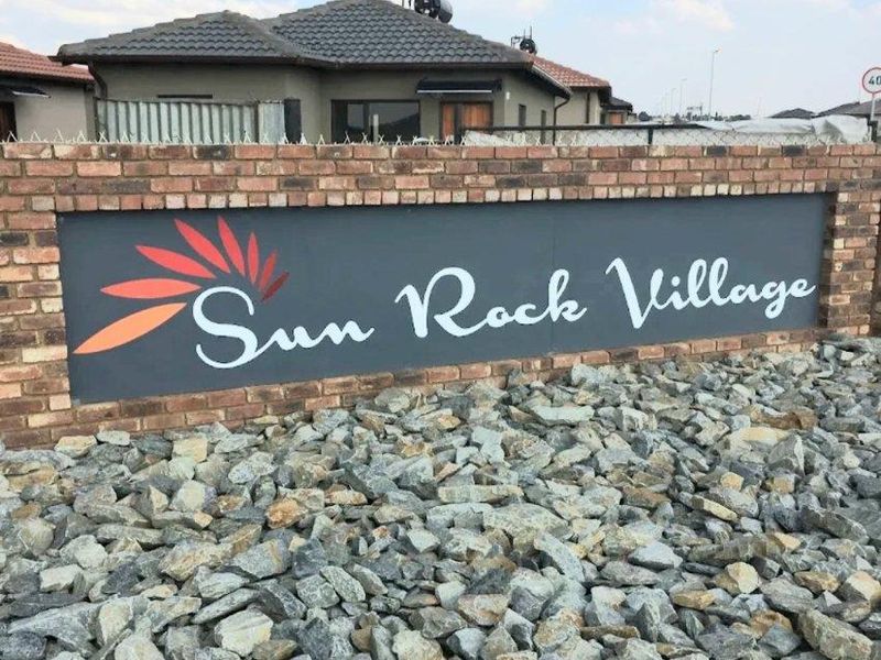 Entrance signage for Sun Rock Village featuring a brick boundary wall and decorative rock landscaping.