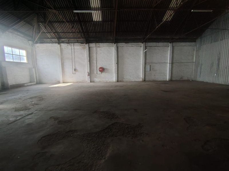 Spacious industrial warehouse unit featuring high ceilings with exposed steel trusses, painted brick walls, and durable concrete flooring.