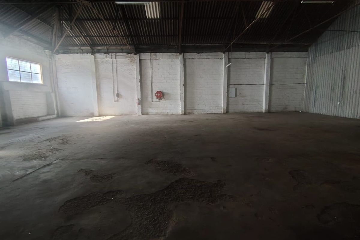 Spacious industrial warehouse unit featuring high ceilings with exposed steel trusses, painted brick walls, and durable concrete flooring.
