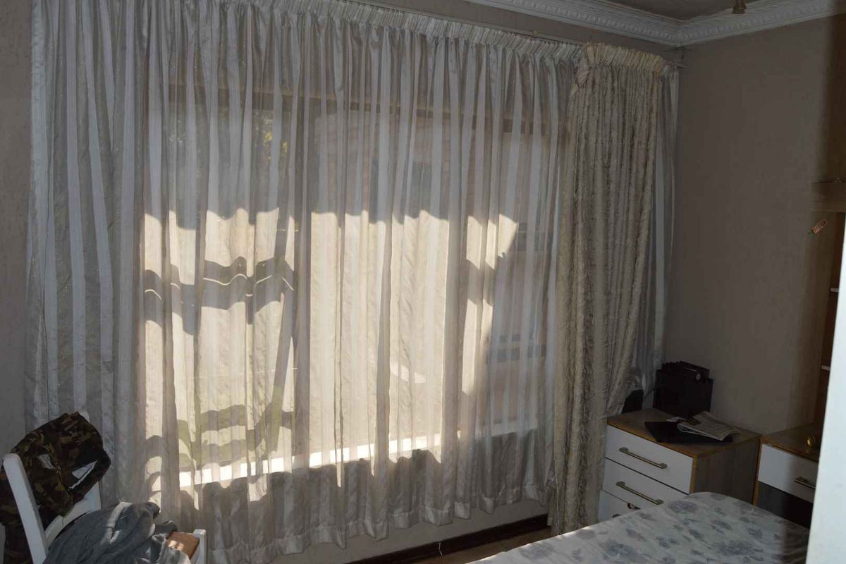 A bedroom featuring large windows with floor-to-ceiling curtains and decorative crown molding.