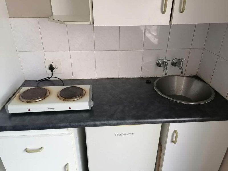 A compact kitchen area featuring a laminate countertop, stainless steel sink, tiled splashback, and built-in cabinetry.