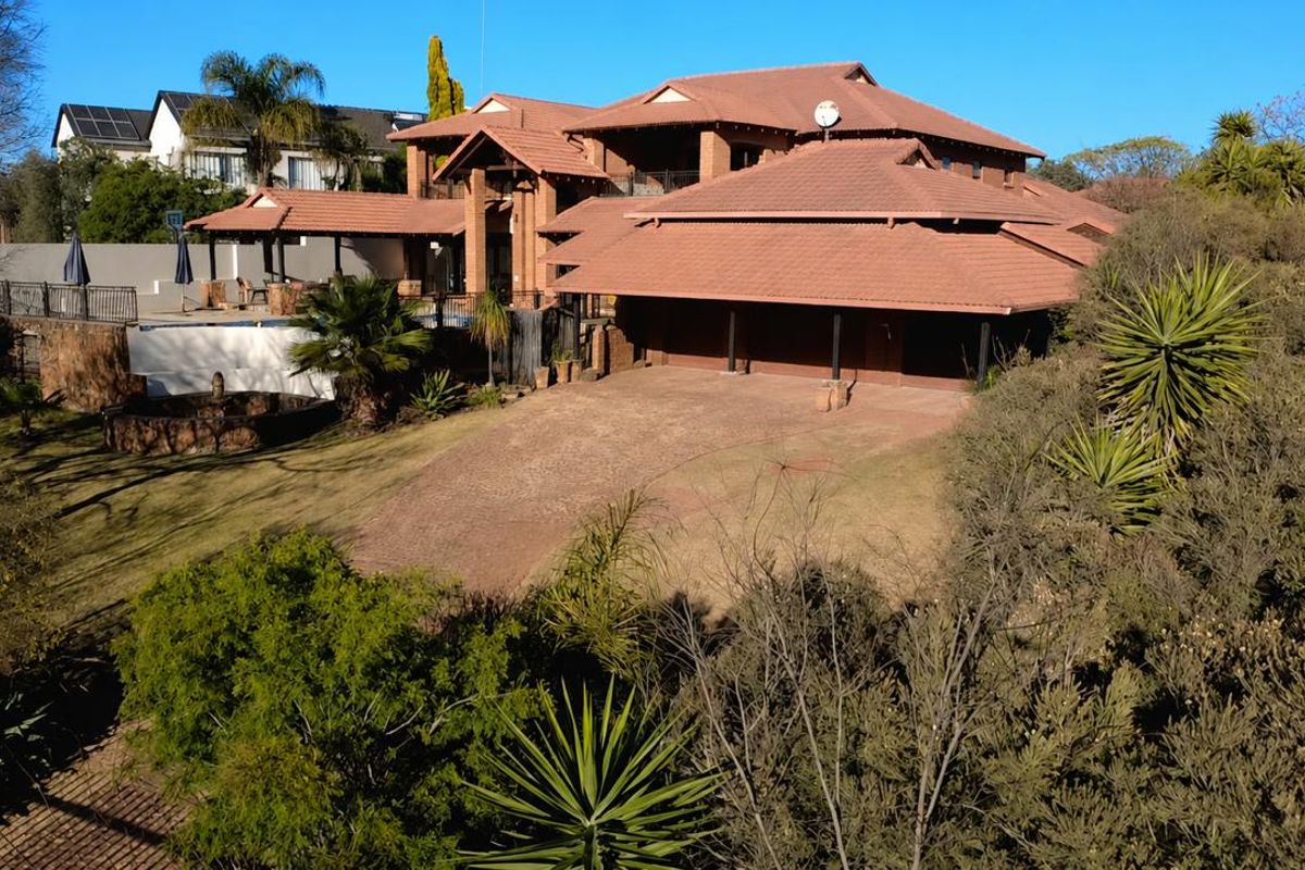Aerial view of a large residential property featuring a multi-car garage, tiled roof, swimming pool, and established garden.