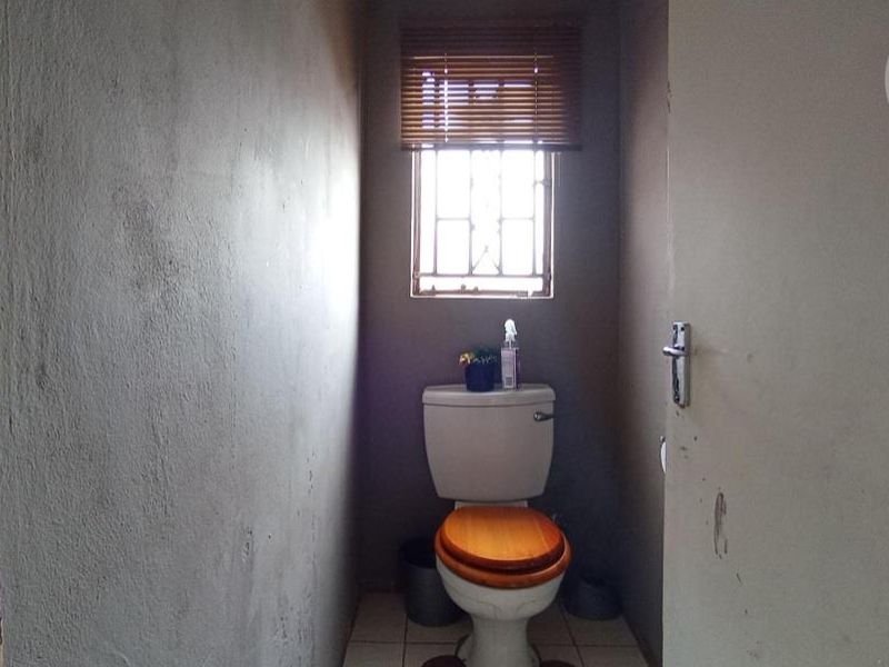 A small, functional bathroom featuring a standard toilet, tiled flooring, and a window with security bars, currently requiring cosmetic updates and wall finishing.