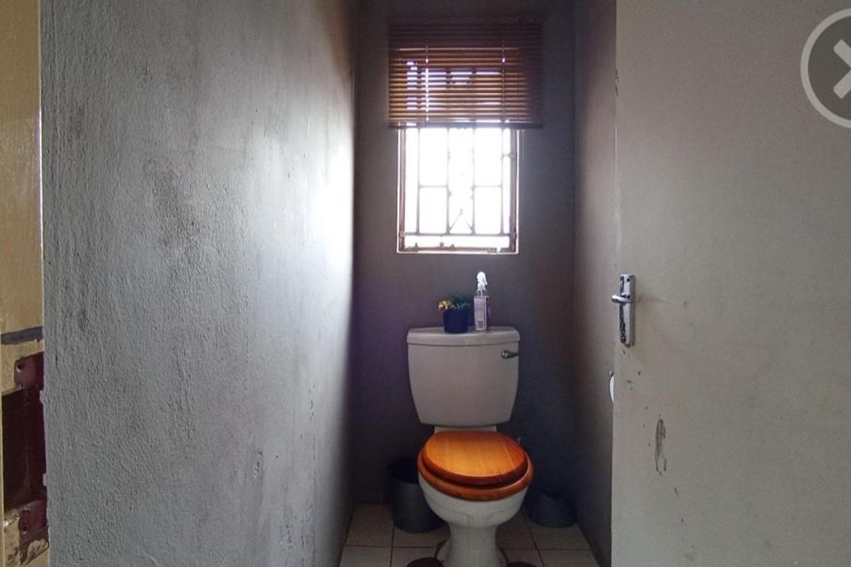A small, functional bathroom featuring a standard toilet, tiled flooring, and a window with security bars, currently requiring cosmetic updates and wall finishing.
