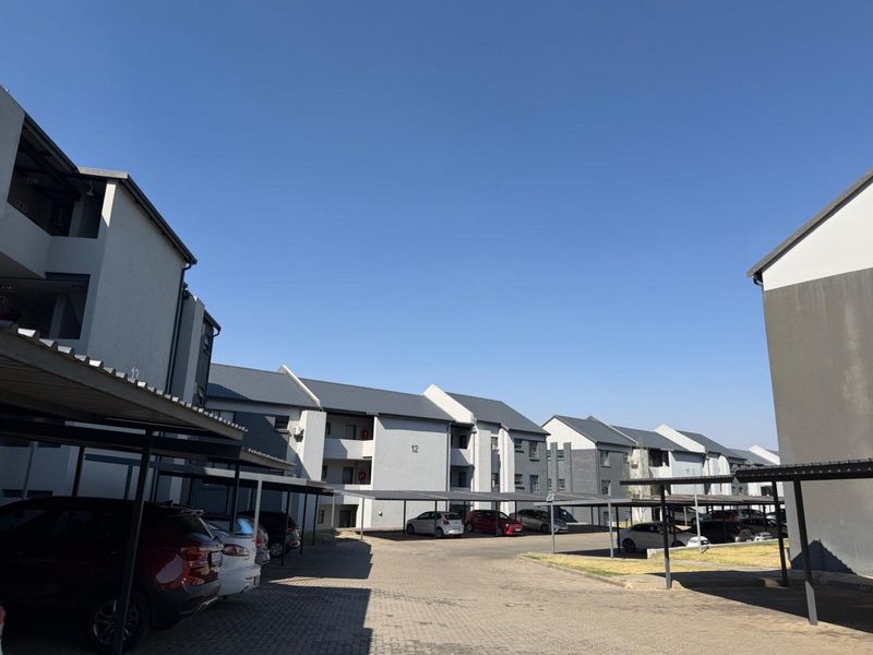 Exterior view of a multi-story apartment complex featuring paved driveways and covered parking bays under a clear blue sky.