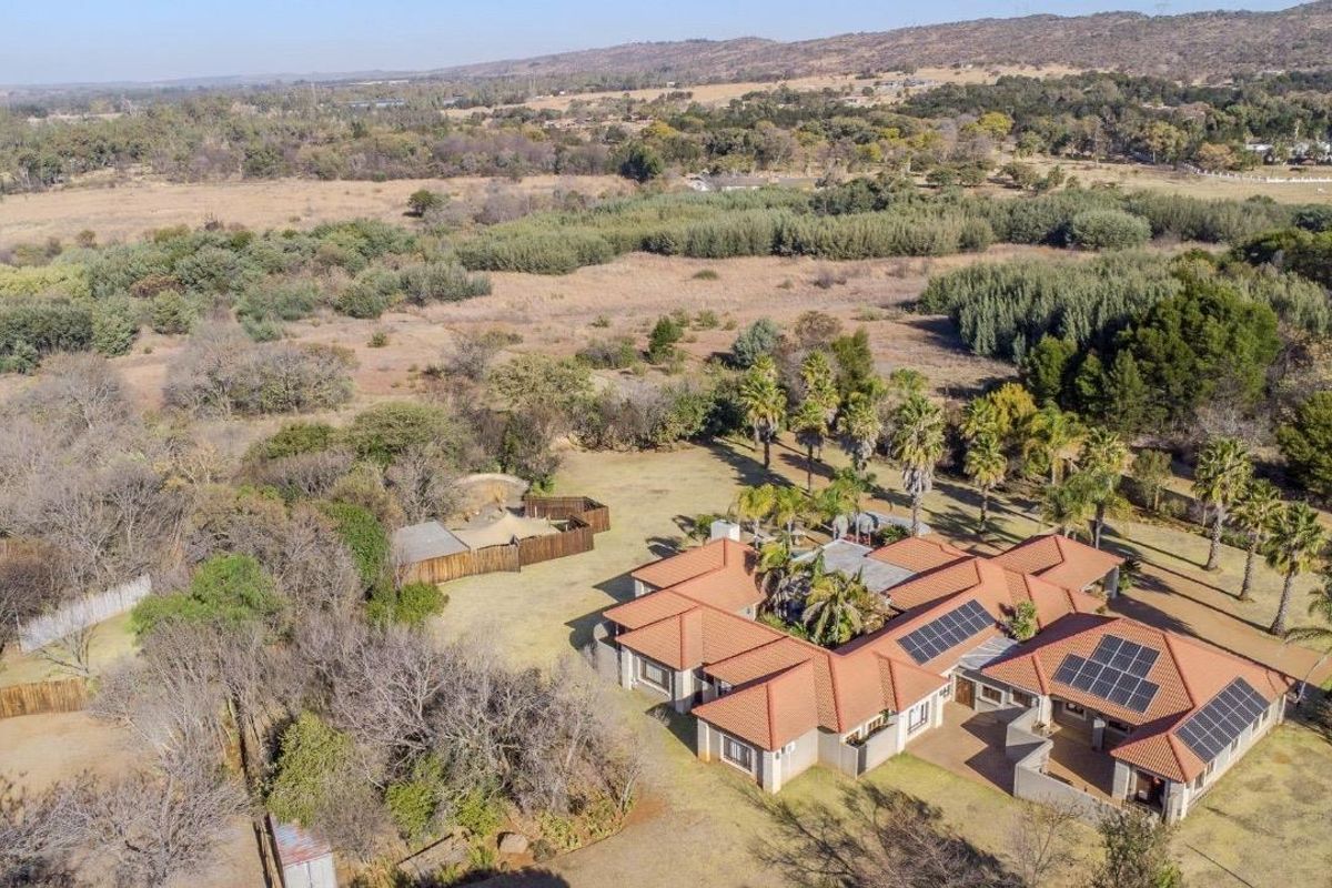 Aerial view of a large residential property featuring a sprawling layout with terracotta tiled roofing, solar panels, and extensive surrounding garden grounds.
