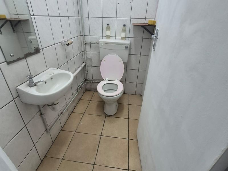 A compact bathroom featuring a wall-mounted basin and ceramic toilet with tiled walls and flooring, requiring cosmetic updates to improve the overall finish.